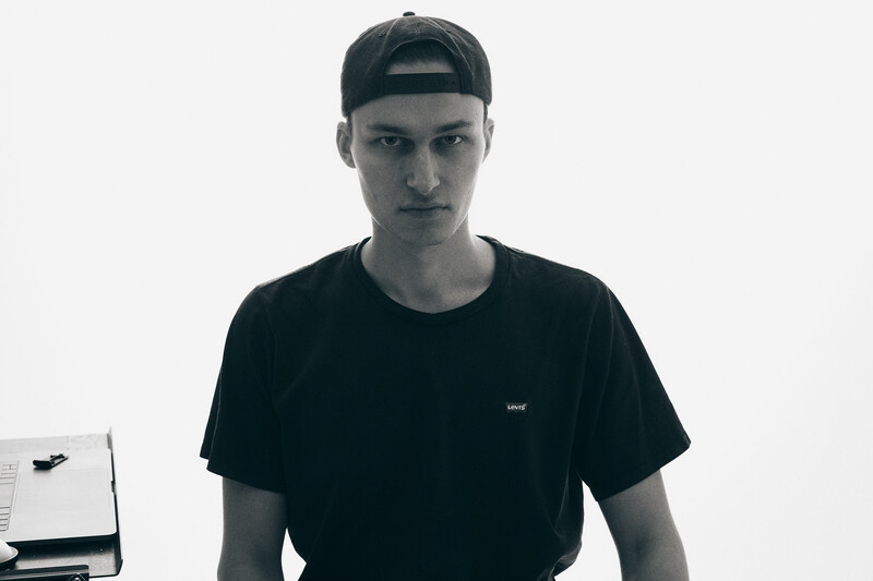 Young man in black t-shirt and cap looking directly at camera against white background.