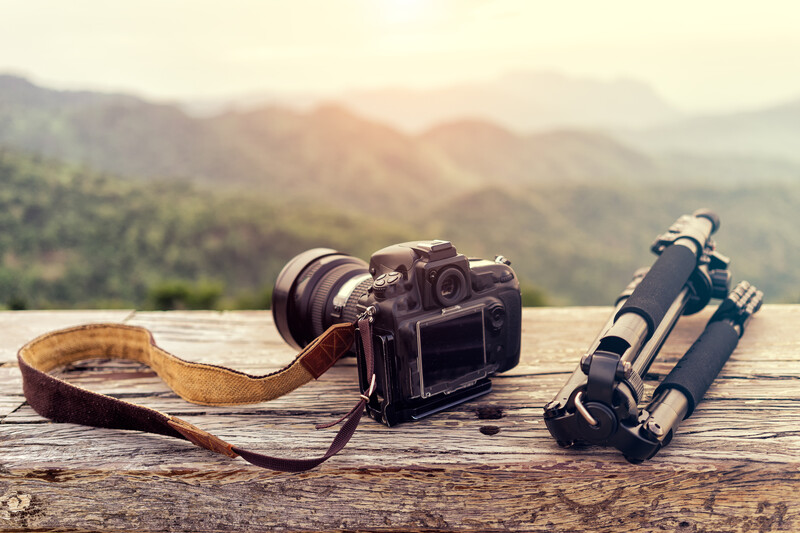 Vintage camera with leather strap and telephoto lens on wooden surface overlooking mountainous landscape.