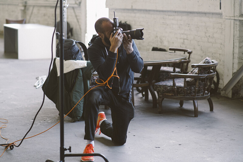 Photographer kneeling while operating a professional camera with telephoto lens in an industrial studio space.
