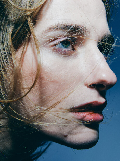 Close-up profile portrait of a person against a blue background with directional side lighting.
