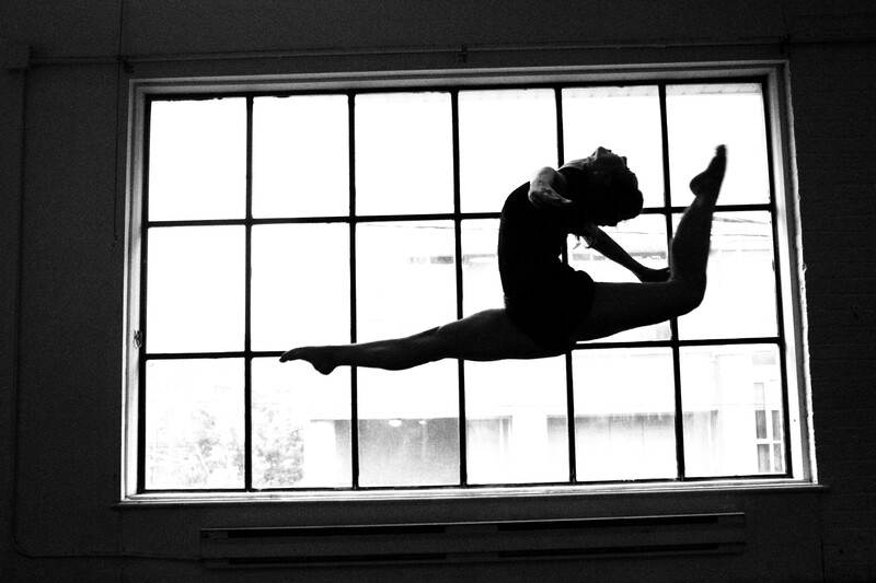 Silhouette of a person performing a horizontal leap in front of a large multi-pane window.