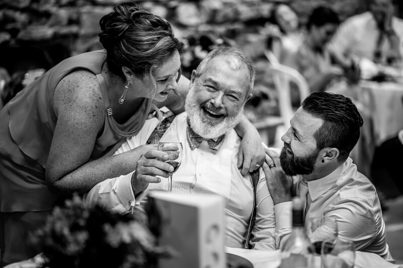 Three people laughing together at an outdoor event, captured in black and white.