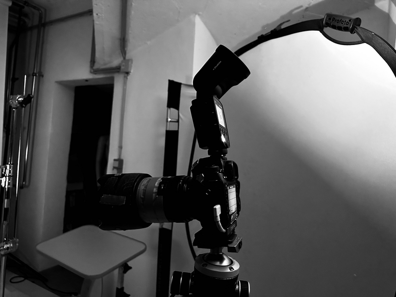 Professional studio lighting setup with camera mounted on tripod and adjustable softbox reflector positioned overhead.