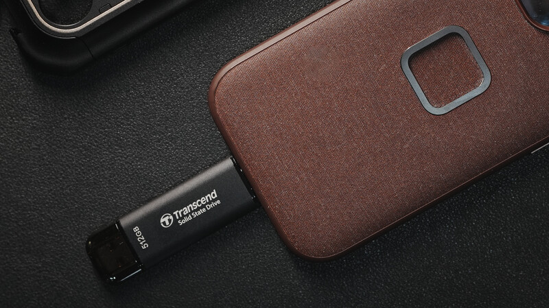 Brown leather phone case with camera cutout next to black USB drive on dark textured surface.