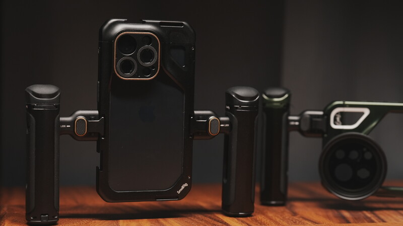 Smartphone with protective case surrounded by camera lens attachments on wooden surface.