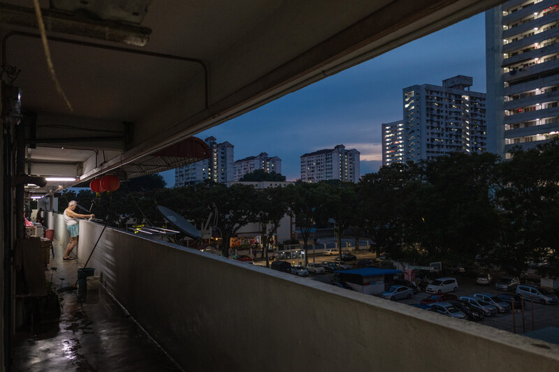 Urban twilight view from covered balcony overlooking residential towers and tree-lined street below.