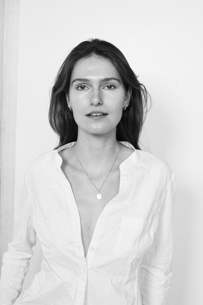 Woman with dark shoulder-length hair wearing a white button-up shirt against a plain white background.