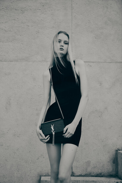 Woman in dark sleeveless dress standing against textured concrete wall.
