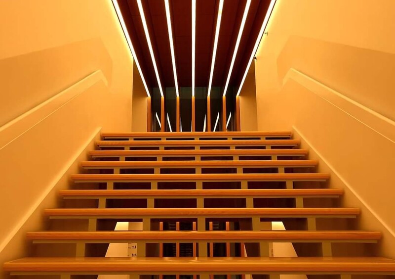 Looking up a symmetrical staircase with warm orange walls and dark wooden railings converging toward ceiling.
