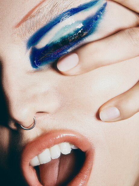 Close-up of a person's face with bold blue eyeshadow and nude nails.