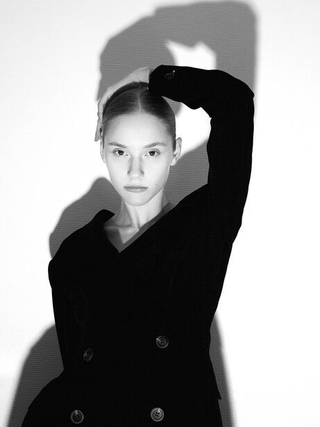 Black and white portrait of a woman in a double-breasted blazer with her arm raised to her head.