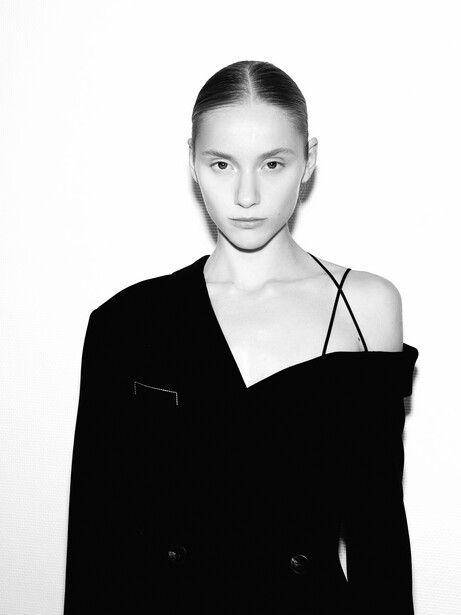 Woman in black blazer and dark camisole against white background in studio portrait.