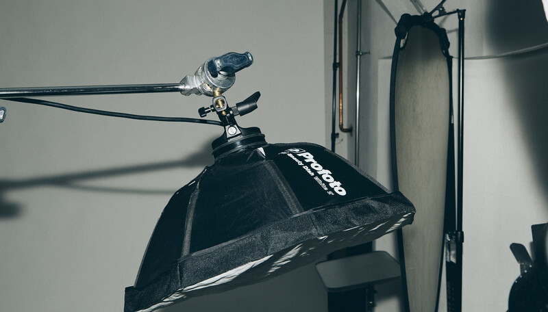 Professional studio lighting setup with a softbox and reflector mounted on stands against a white wall.