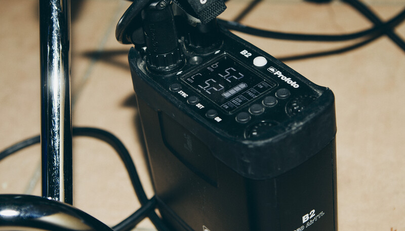 Black audio mixer or control surface with illuminated buttons and dials on a beige surface with coiled cables.