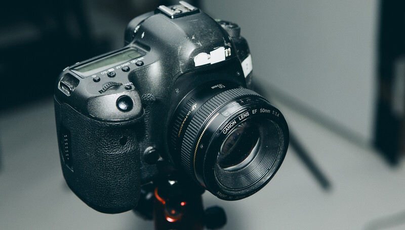 Professional DSLR camera with prime lens mounted on a tripod head against neutral background.