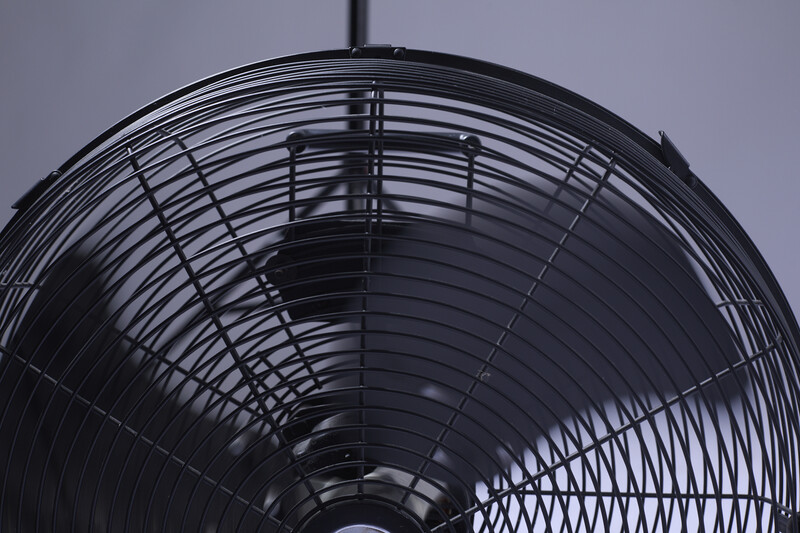 Close-up of a black oscillating fan's protective cage and blades against a light gray background.