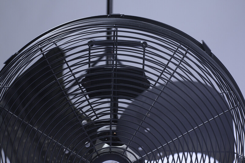 Close-up view of a black oscillating fan's grille and blade structure against a light sky.