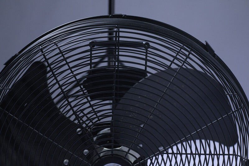 Close-up view of a black oscillating fan's grille and blades against a gray sky.