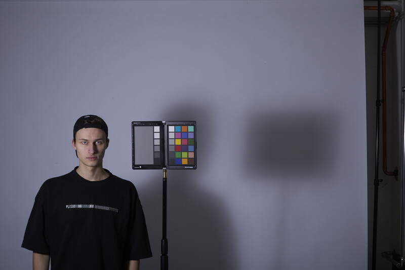 Portrait of a young man standing in front of a color checker chart and studio lighting setup against a gray wall.