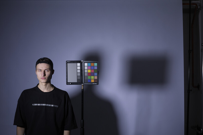 Portrait of a man in black shirt next to studio lighting setup with color checker and reflector.