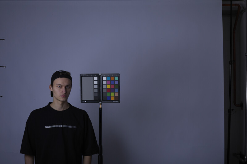 Portrait of a man against a blue-gray wall with a color checker chart mounted on a stand beside him.