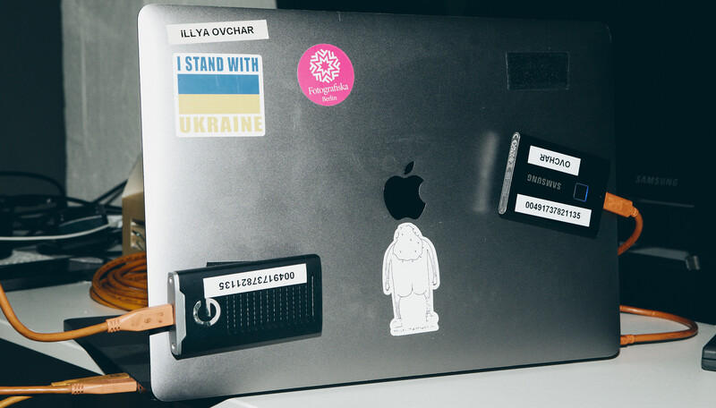 MacBook laptop decorated with stickers including a Ukraine solidarity badge and minimalist illustrations.