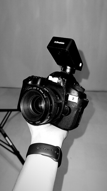 Hand holding a professional video camera with external flash mounted on top against gray background.