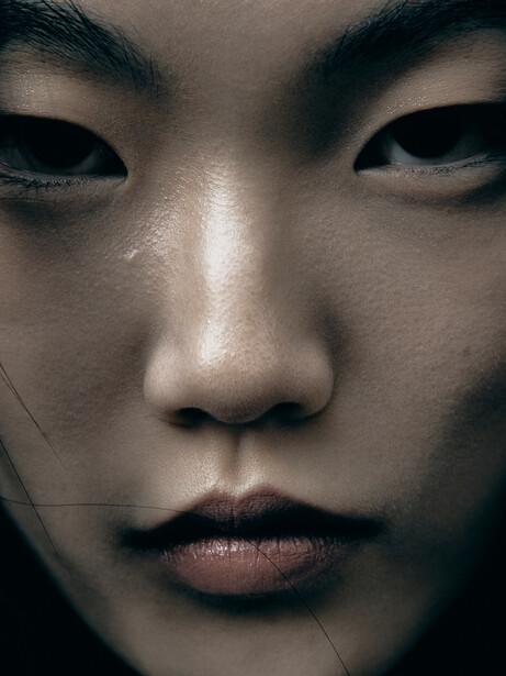 Close-up portrait of a person's face with downward gaze and neutral expression.