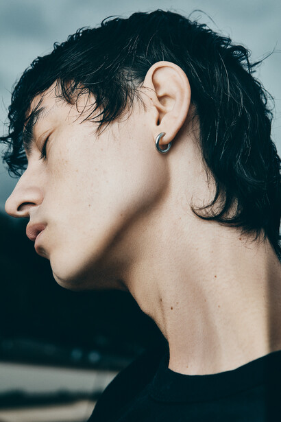 Profile view of a person with dark hair wearing a black shirt against a muted sky backdrop.
