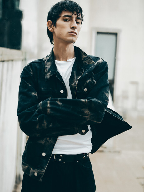 Person wearing a black patterned blazer and white shirt against a minimalist urban backdrop.