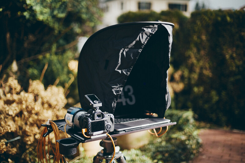 Professional cinema camera mounted on tripod with large black matte box in sunlit garden setting.