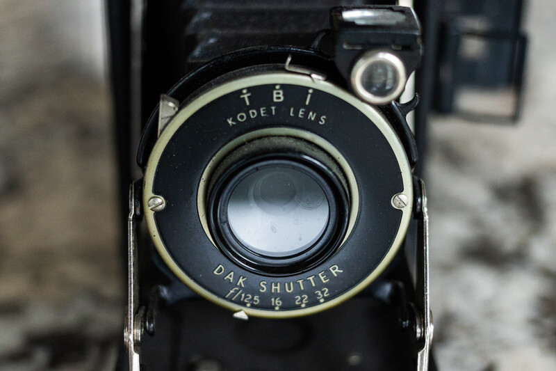 Close-up of a vintage folding camera with Kodet lens and Dak shutter mechanism on black body.