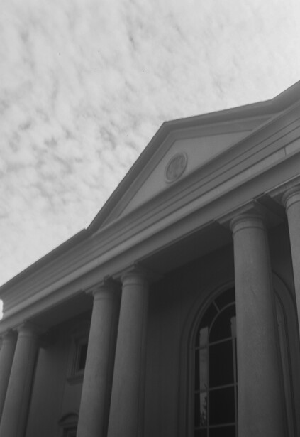 Classical building facade with tall columns and a pediment against an overcast sky.