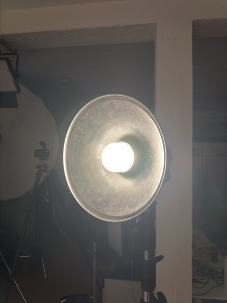 Studio softbox with bright central light source mounted on stand in dimly lit interior space.