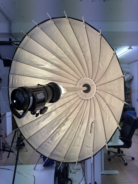 Large white parabolic reflector with mounted camera and lens in studio setting.