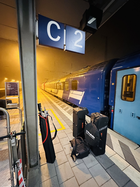 Passenger waiting on train platform at night with blue train and illuminated platform sign.