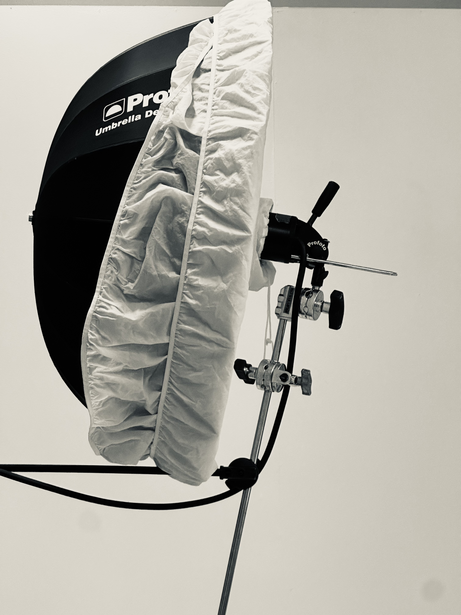 Studio lighting setup with white umbrella diffuser and black reflector mounted on stand.