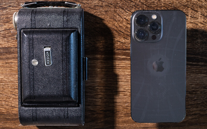 Vintage leather camera case and modern iPhone 14 Pro positioned side by side on wooden surface.