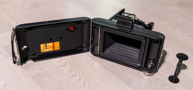 Vintage folding camera disassembled showing back plate, film chamber, and separated viewfinder component.