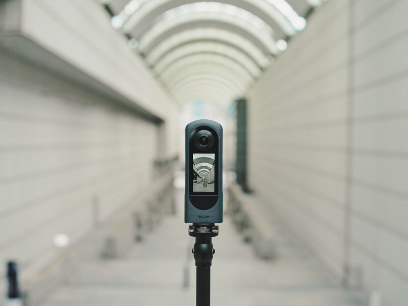 A camera mounted on a tripod in the foreground, pointed down a long symmetrical corridor with arched white ceiling.