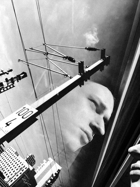 Black and white photograph of a man's face overlaid with geometric lines and antenna structures creating a surreal composite.