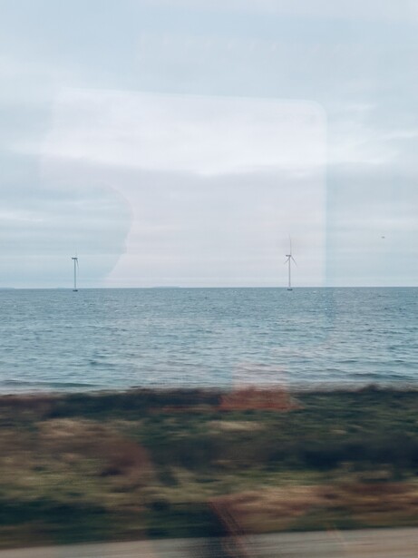 Seascape with wind turbines visible on the horizon across calm ocean waters.