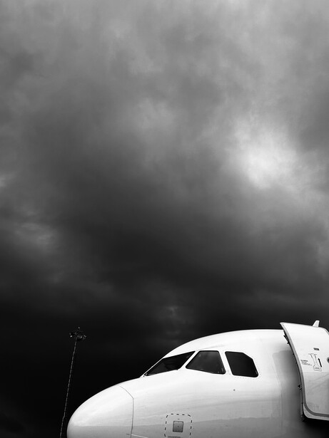 Commercial aircraft nose against dark, dramatic storm clouds.