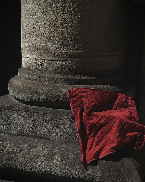 Red fabric draped against a concrete cylindrical column with dramatic side lighting.
