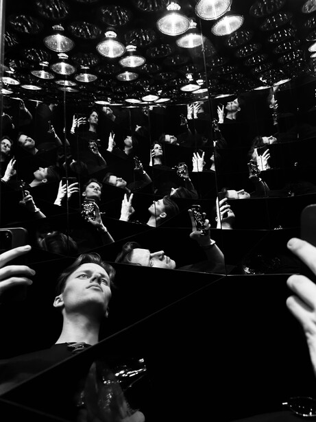 Dramatic black and white portrait of a person looking upward surrounded by raised hands and faces of a crowd.