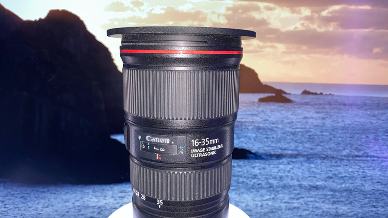 Canon 16-35mm telephoto lens displayed against a scenic coastal landscape at sunset.