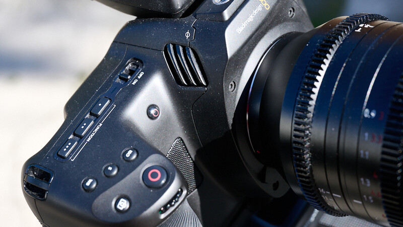 Close-up of professional cinema camera body with mounted lens and control buttons visible.