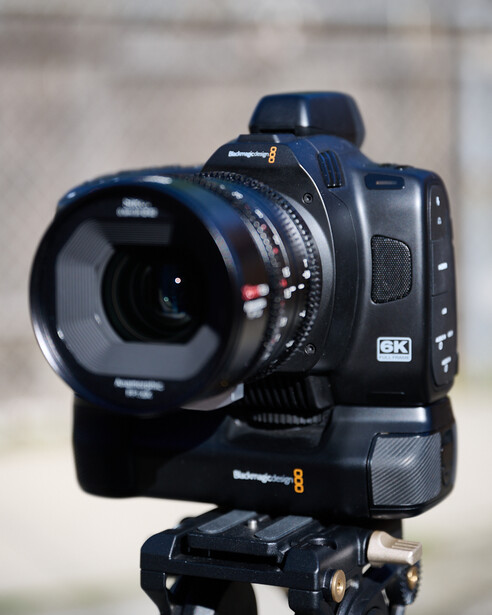 Black cinema camera with wide-angle lens mounted on tripod with follow focus system.