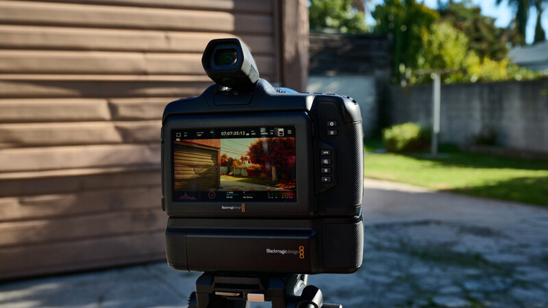 Blackmagic camera mounted on tripod displaying footage on rear monitor in outdoor residential setting.