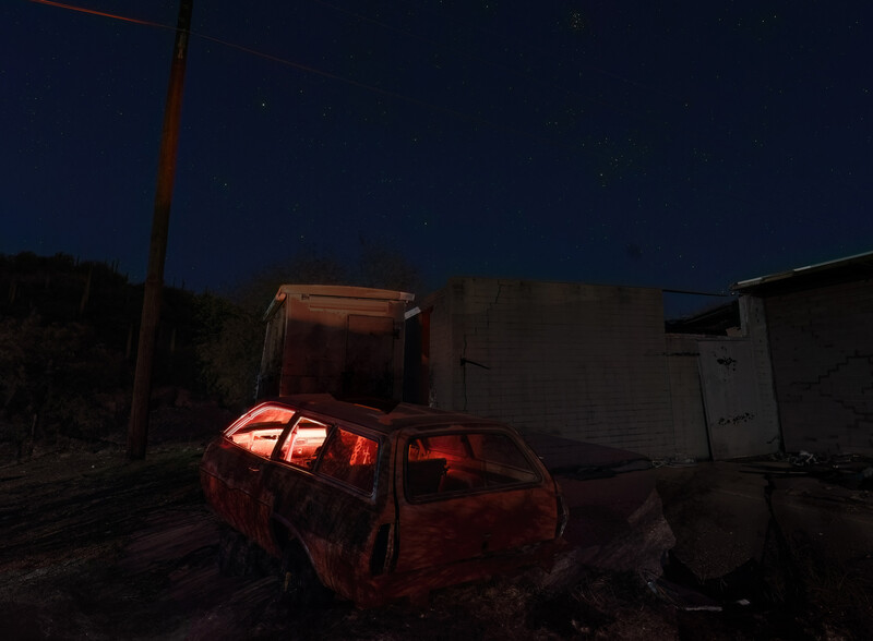 Abandoned red vehicle with open cargo bed illuminated by headlights at night.